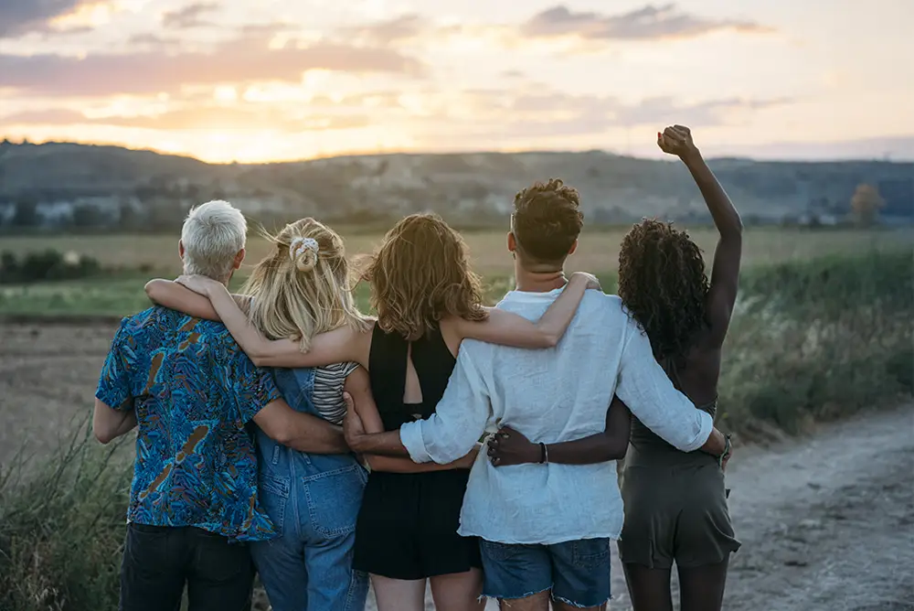 Grupo de personas abrazadas contemplando un atardecer en el campo